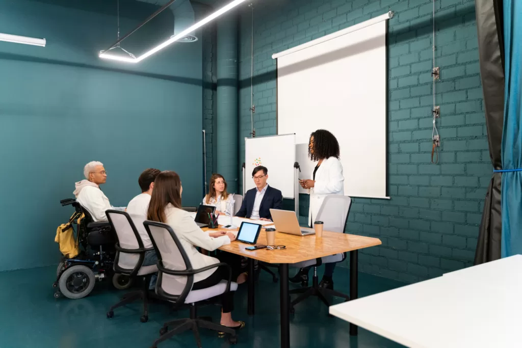 Black businesswoman with curly hair standing near a whiteboard speaking during a team meeting in a conference room